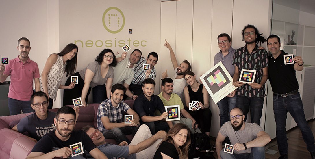 El equipo de Visual tags posa en la oficina de Neosistec. Cada uno lleva un tag en la mano. Son 18 personas y un perro guía.